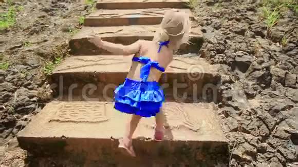 背面小金发女孩攀登公园的高石台阶视频的预览图