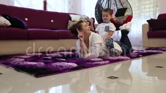 一位年轻的母亲和她的小儿子躺在客厅的地板上看电视视频的预览图