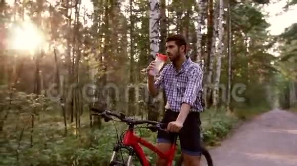 年轻的帅哥坐在自行车上喝水视频的预览图