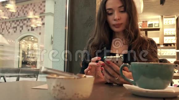 漂亮的年轻女人在咖啡馆里用她的智能手机4K视频视频的预览图