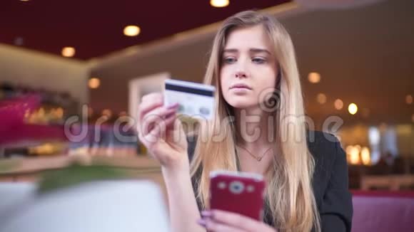 穿黑色夹克的金发女郎在咖啡馆A她在智能手机上的银行卡数据方面处于领先地位视频的预览图