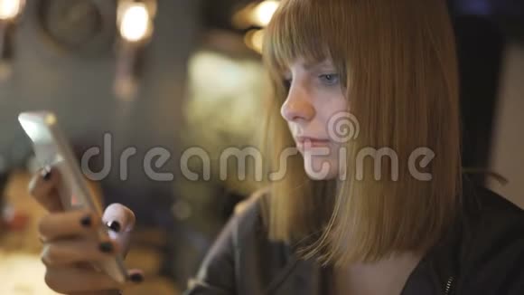 年轻漂亮的红发女人坐在咖啡馆或酒吧里用智能手机视频的预览图