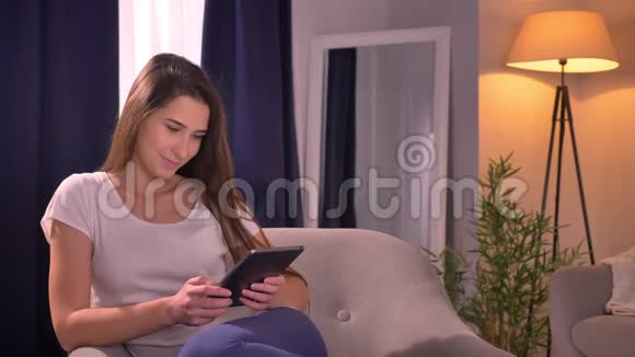 一位年轻迷人的白种人女性的特写肖像她用平板电脑坐着看着镜头微笑视频的预览图