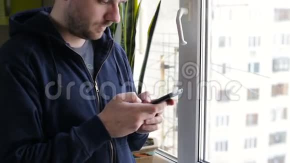 年轻快乐的男人在家靠窗在智能手机上发短信视频的预览图