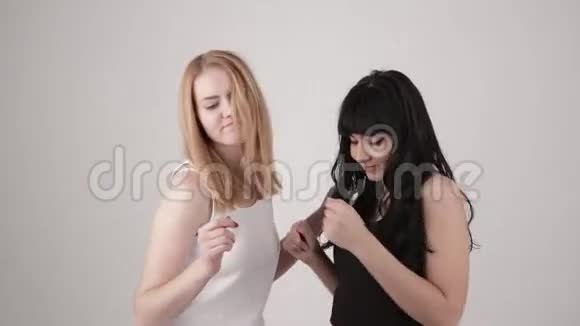 两个快乐的女孩黑发和金发在浅灰色的背景下慢慢地在室内跳舞复制空间文本视频的预览图