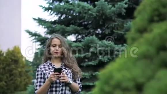 一个留着长发的漂亮女孩在树的背景下使用电话视频的预览图