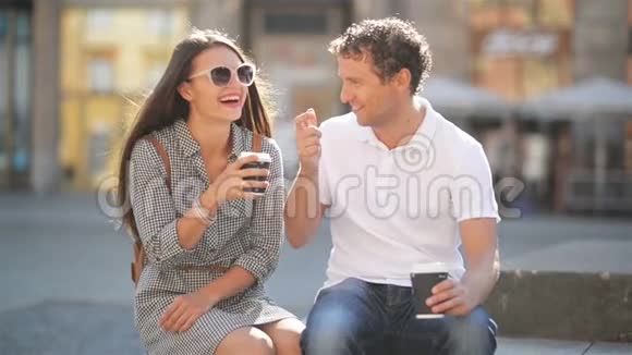 快乐的朋友在阳光明媚的夏日坐在城市广场的长凳上喝咖啡视频的预览图