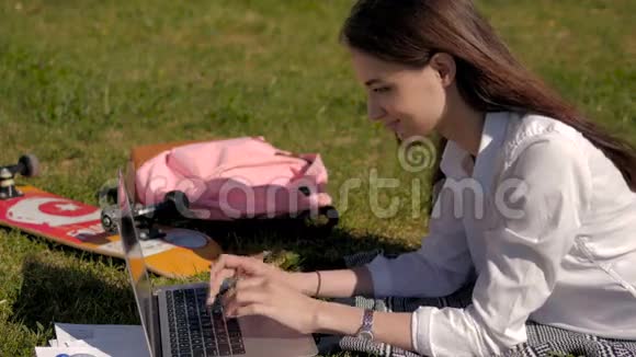 一个年轻学生在公园草地上躺着时使用她的笔记本电脑的侧视图视频的预览图
