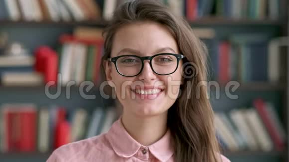 在图书馆书架背景下年轻漂亮的图书管理员女士微笑着开心地看着相机视频的预览图