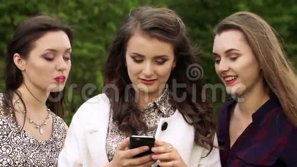 三个年轻女孩看着电话对大自然微笑慢慢地视频的预览图