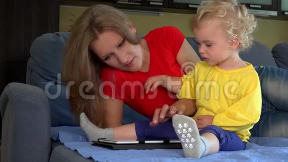 微笑的女人教小蹒跚学步的女孩使用平板电脑坐在床上视频的预览图