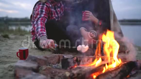 一对相爱的情侣坐在湖边的篝火旁聊天喝着热茶煎着棉花糖视频的预览图