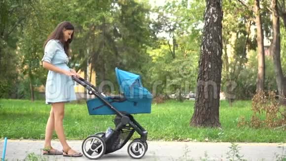 妈妈带着婴儿车在公园里散步夏季自然背景视频的预览图
