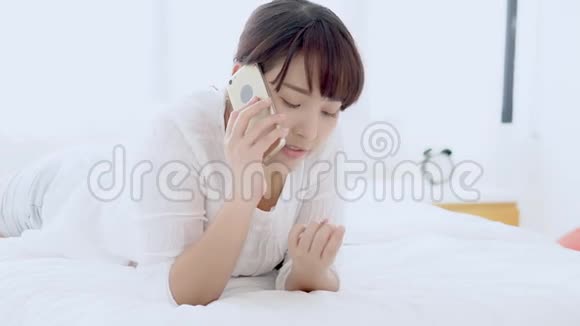 美丽的年轻亚洲女人微笑着躺在卧室里放松女孩用手机聊天享受和乐趣视频的预览图