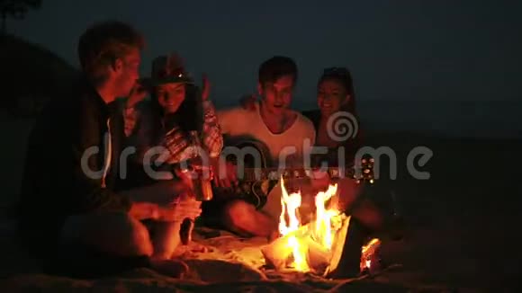 晚上在海滩上用篝火野餐年轻人快乐的朋友唱歌弹吉他视频的预览图