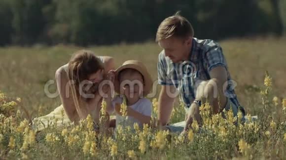 快乐的小男孩和他的父母坐在绿色的草地上视频的预览图