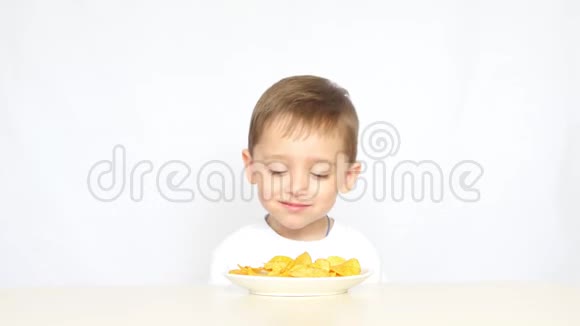一个喜欢吃薯片的孩子坐在一张白色背景的桌子旁视频的预览图