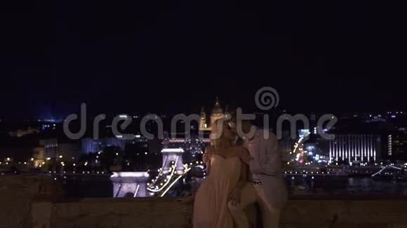 华丽性感的新婚夫妇晚上在城市桥上亲吻和拥抱夜间婚礼视频的预览图