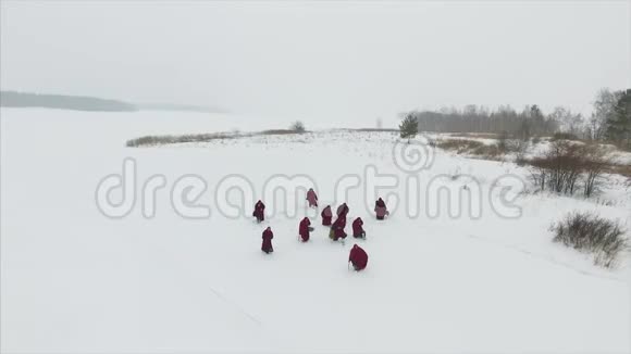 一群穿着头巾的僧侣在森林中的冬季雪道上行走鸟瞰录像视频的预览图
