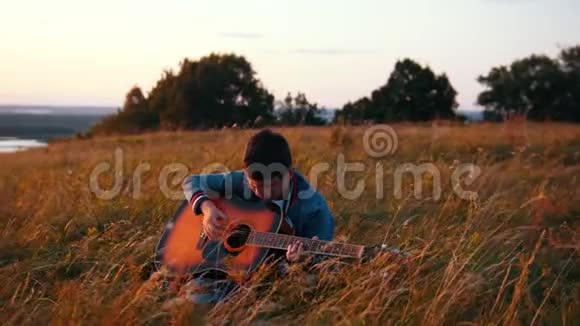 戴着圆眼镜的男孩在日落时分的田野里弹吉他视频的预览图
