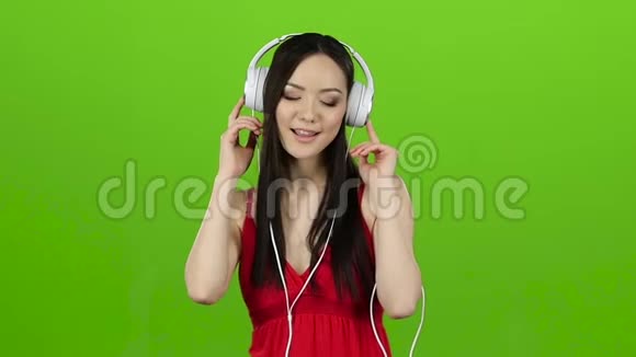 女孩通过耳机听欢快而充满活力的音乐绿色屏幕慢动作视频的预览图