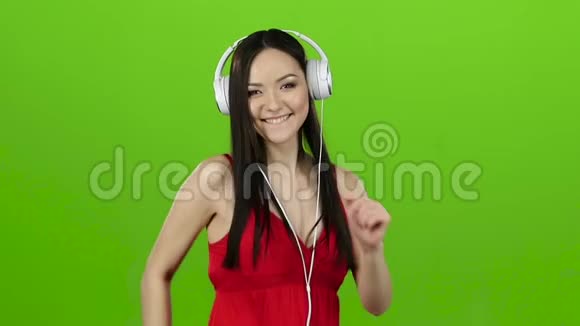女孩通过耳机听欢快而充满活力的音乐绿色屏幕慢动作视频的预览图