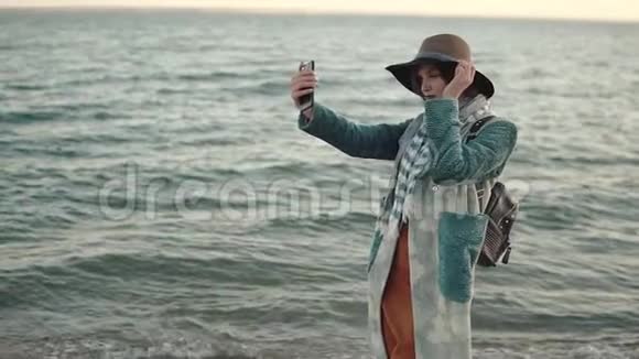 日落时在海滩上自拍的女孩一位身穿秋装的年轻漂亮女子在手机上拍照视频的预览图