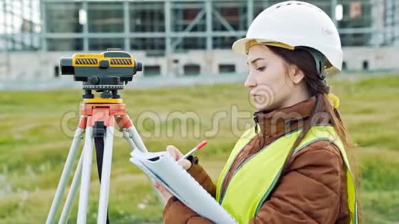 一位穿着工作服和头盔的年轻女性测量员调整设备并对建筑进行计算视频的预览图