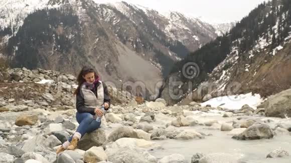 美丽的女旅行者在山的背景下的一条山河旁喝水视频的预览图