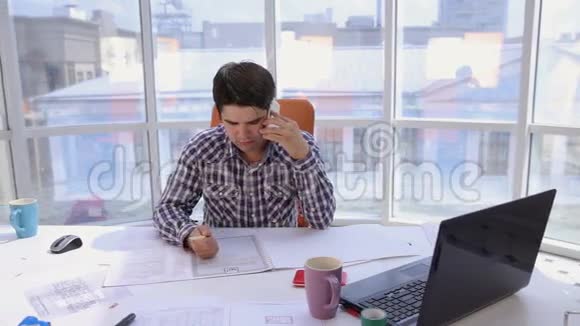 一个自信而有魅力的商人用蓝图工作在一个轻盈现代化的办公室里打电话商务视频的预览图
