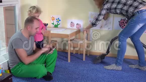 懒惰的父亲和小女儿使用平板电脑和母亲胡佛地板视频的预览图