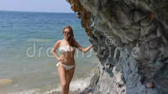 性感的年轻女子戴着太阳镜和白色比基尼的长发站在海边靠近大海视频的预览图