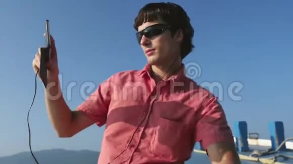 年轻迷人的戴着耳机和手机的太阳镜在游轮旅行时听音乐视频的预览图