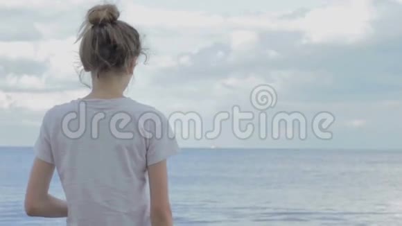 年轻的女孩穿着白色T恤头发被绑起来用戏剧性的夜空向大海投掷石头视频的预览图
