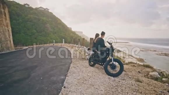 一个年轻的女人和她的男朋友骑手和他的摩托车一起欣赏周围的美丽景色山和视频的预览图