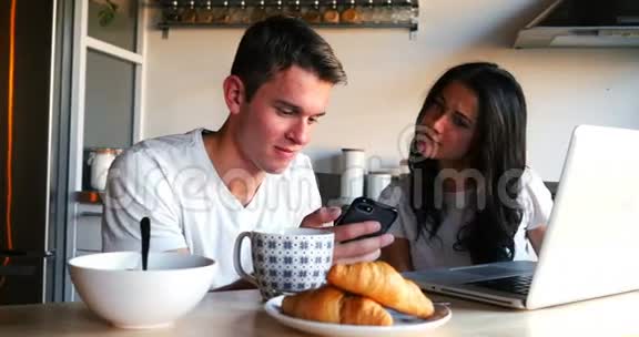 夫妇在吃早餐时使用手机和笔记本电脑视频的预览图