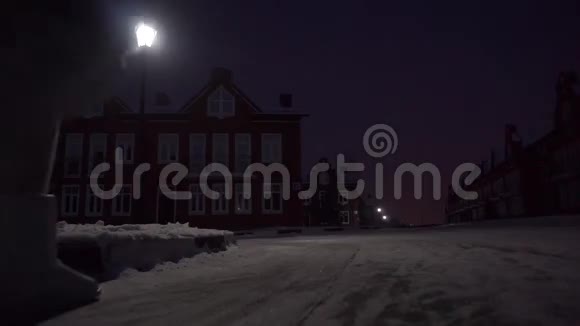 一位穿着毛皮大衣的年轻女子晚上在住宅区的脆雪上散步视频的预览图