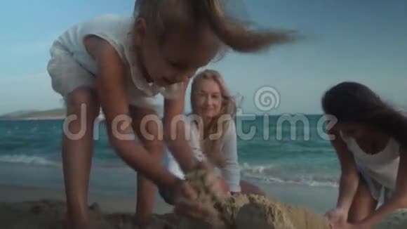 快乐的母亲和女儿在南海海滩上建造了一座沙堡慢动作股票录像视频的预览图