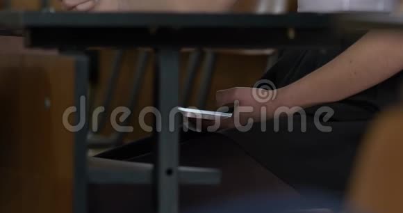 女人在木桌下用智能手机考试期间女人用你的手机上网视频的预览图