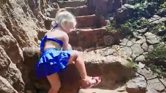 背面小金发女孩攀登公园的高石台阶视频的预览图