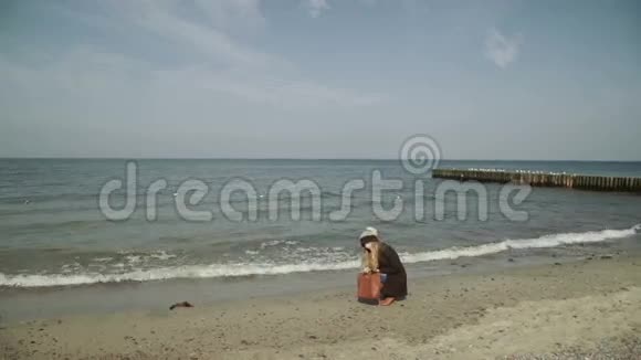 一个女人坐在沙滩上看着鹅卵石海鸥在海上飞翔和游泳视频的预览图