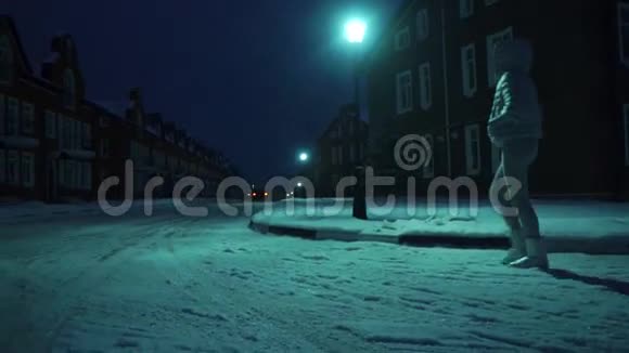 一个穿着银色冬衣的孤独女孩晚上在居民区的雪地上散步视频的预览图