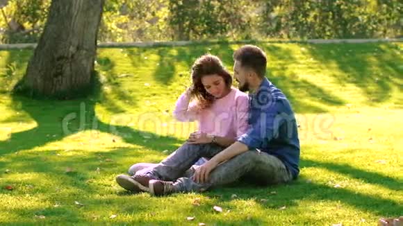 在阳光明媚的日子里一对浪漫的情侣坐在绿色的草地上视频的预览图