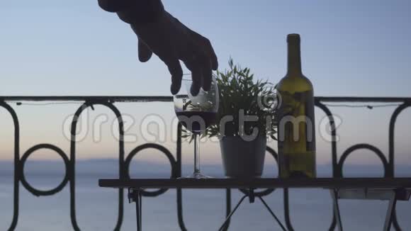 一个男人坐在阳台上在大海的背景上喝红酒特写镜头视频的预览图