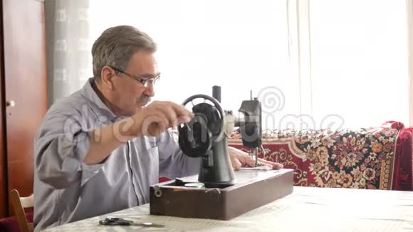 一个有胡子的成年男子在一台旧的手工缝制机器上缝制戴眼镜缝白布视频的预览图