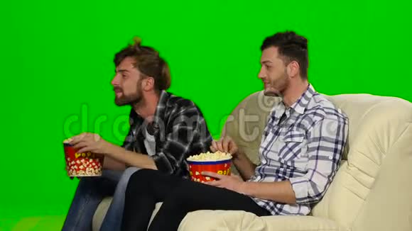 在沙发上看电影吃爆米花的男人绿色屏幕视频的预览图