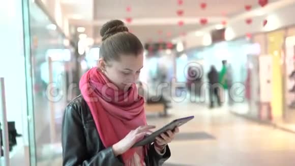 年轻女孩用平板电脑在购物中心微笑的室内4K视频的预览图