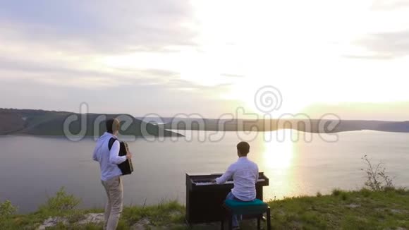 两位音乐家钢琴家和手风琴手在海上日落时在岩石上演奏视频的预览图