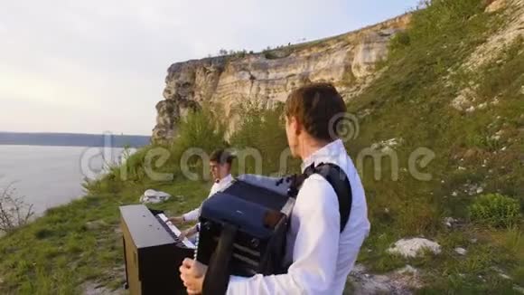 两位音乐家钢琴家和手风琴手在海上日落时在岩石上演奏视频的预览图