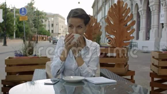 快乐忧郁的女人在街边的咖啡店露台上喝酒视频的预览图